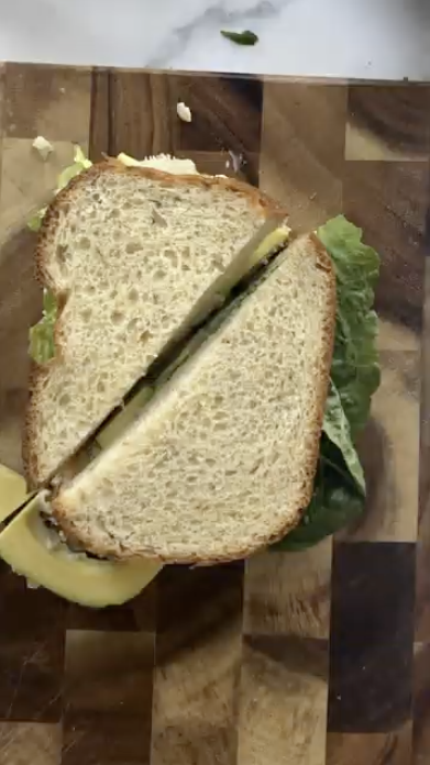 Fresh sandwich with whole wheat bread, lettuce, and avocado, cut in half on a wooden board. Order on Gopuff.