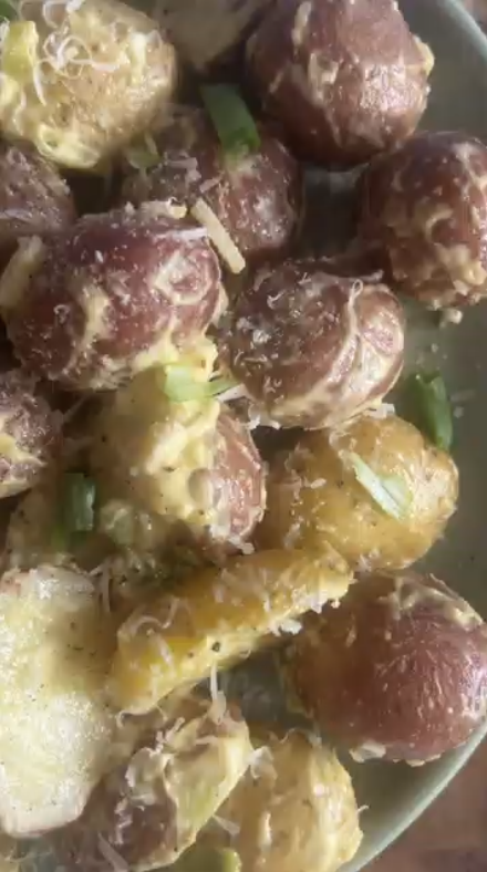 Smashed red potatoes with creamy sauce, grated cheese, and green onions.