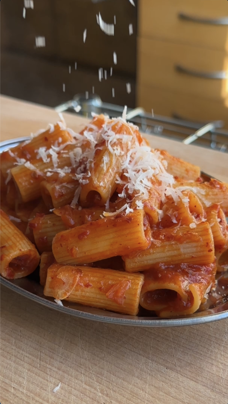Rigatoni pasta with red sauce and grated cheese being sprinkled on top. Order fresh meals from Gopuff.
