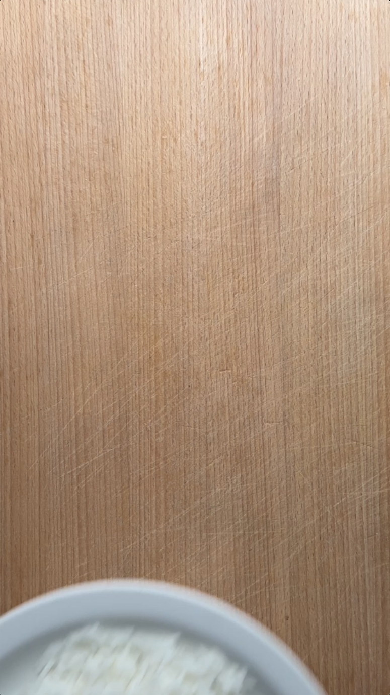Wooden cutting board texture with a blurry white bowl at the bottom.