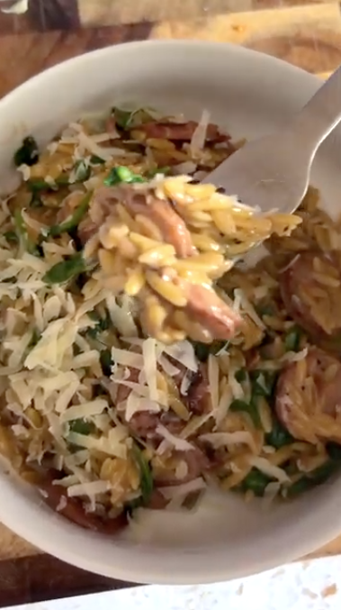 Gopuff orzo pasta meal with sausage, greens, and grated cheese on a fork.