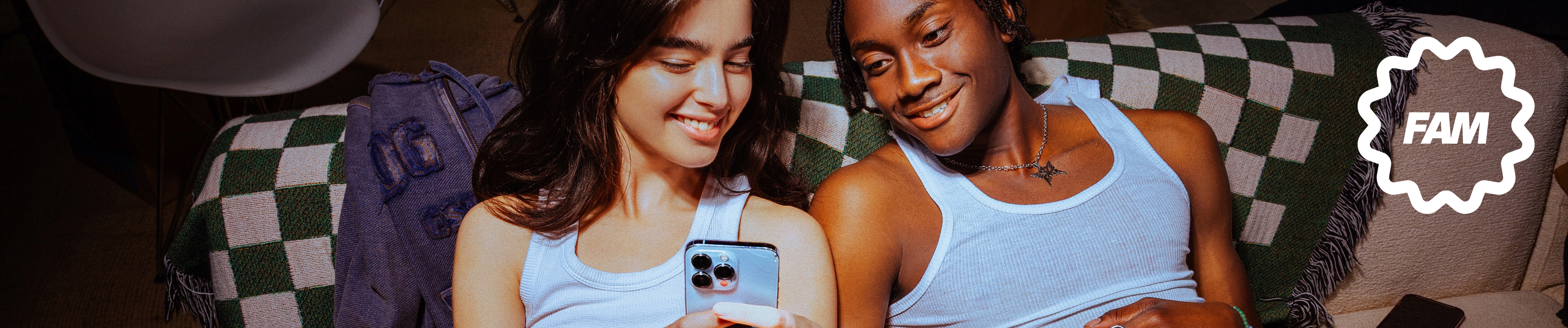 Two friends relaxing on a couch looking at an iPhone with FAM membership badge displayed.