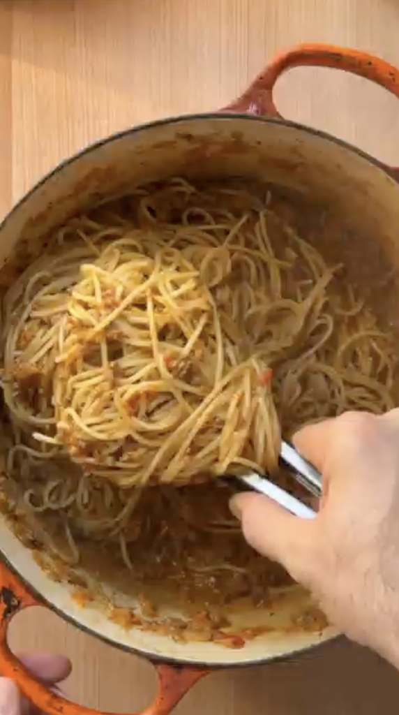 Hand serving spaghetti with meat sauce from an orange pot. Get pasta ingredients delivered by Gopuff.