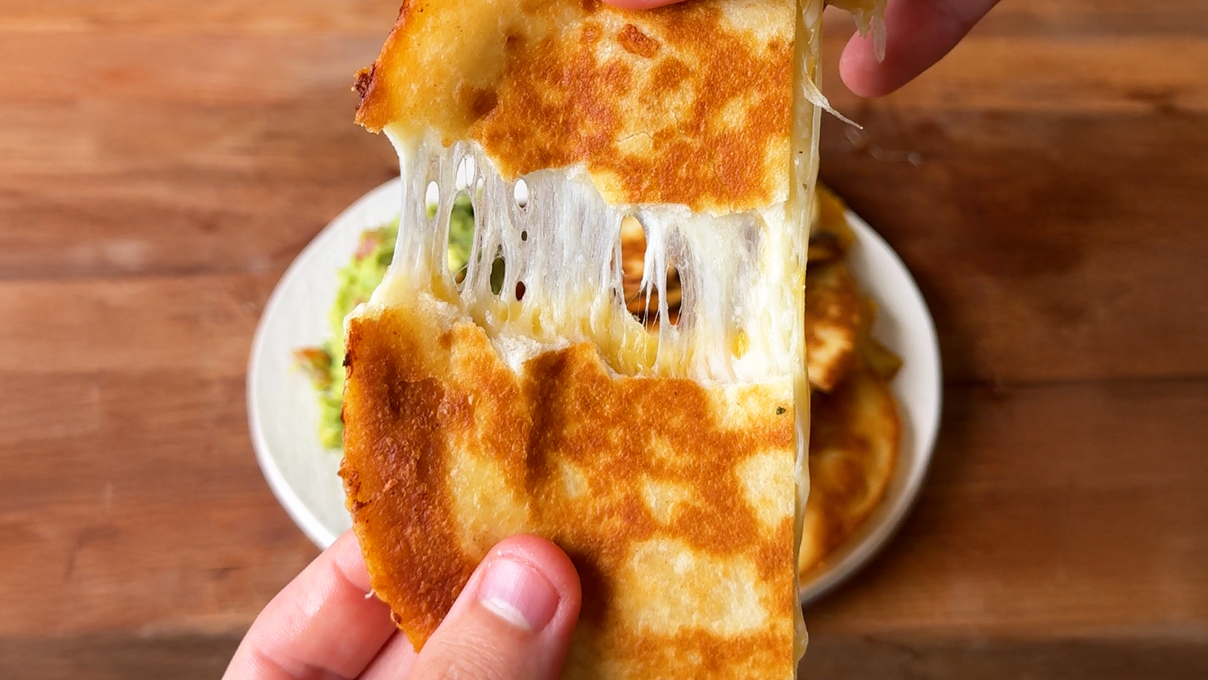 Gopuff: Hand pulling apart a cheesy quesadilla with melted cheese stretching, served with guacamole. Order now!