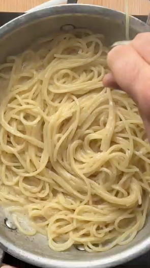 Hand stirring creamy spaghetti in a pot. Get fresh pasta ingredients delivered by Gopuff.