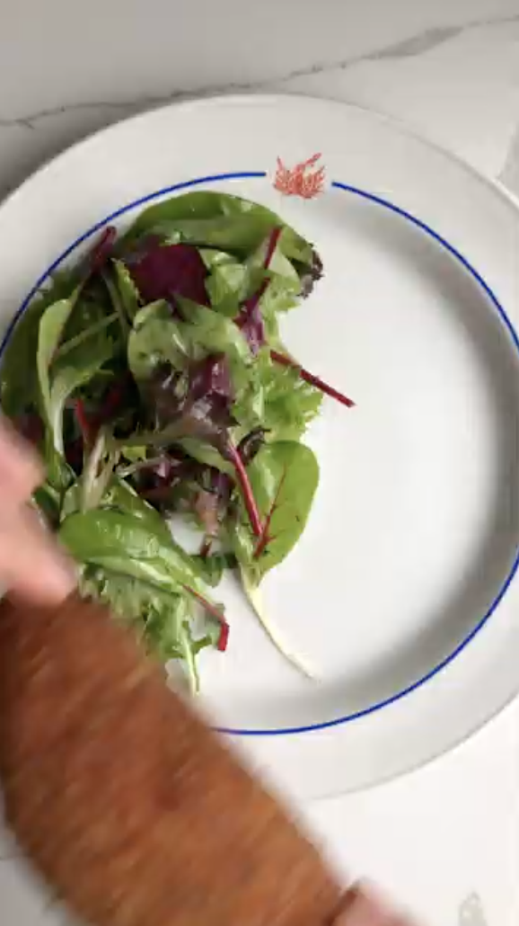 Gopuff meal: Hand placing golden-brown breaded fish fillet next to fresh mixed green salad on a white plate.
